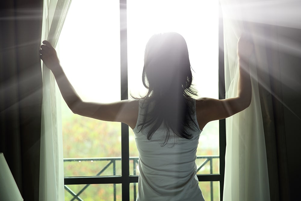 woman opening curtains sunny day