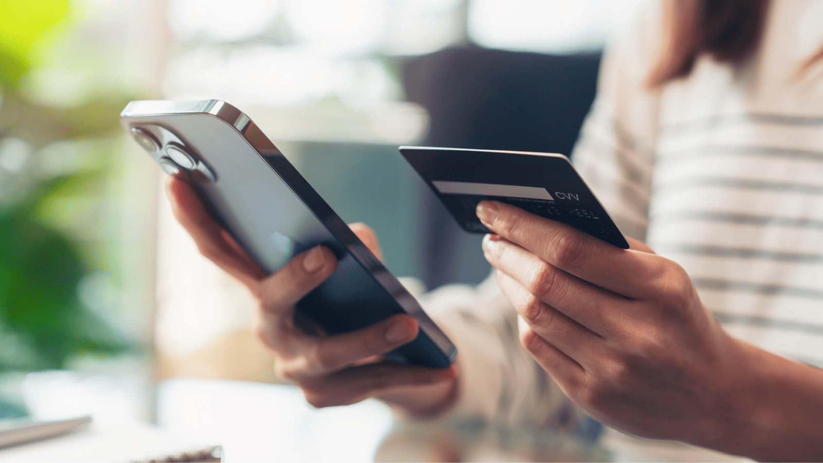 close up of woman's hands. one hand holding a phone and the other holding a debit card