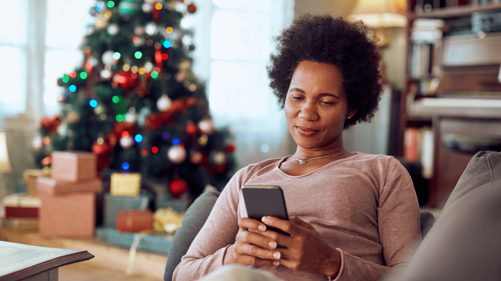 A woman sat on the sofa on her phone with a Christmas tree in the background