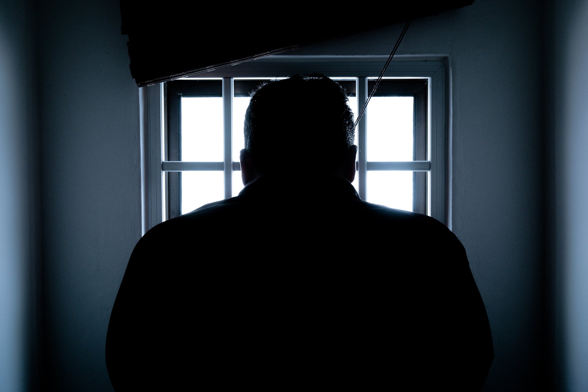 silhouette of man in front of a barred window