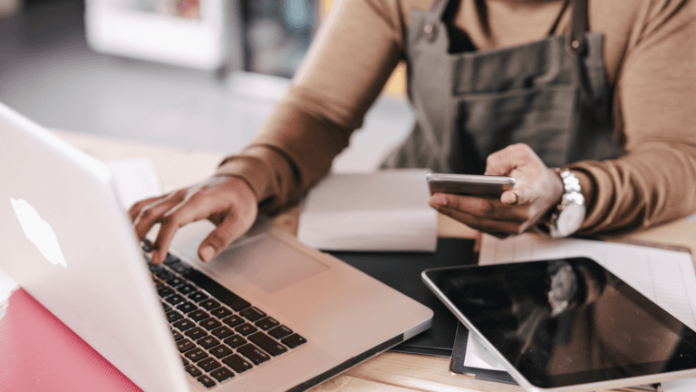 person holding phone and typing on laptop