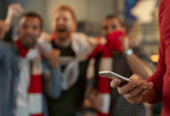 group of friends watching the football and celebrating with one person on their phone