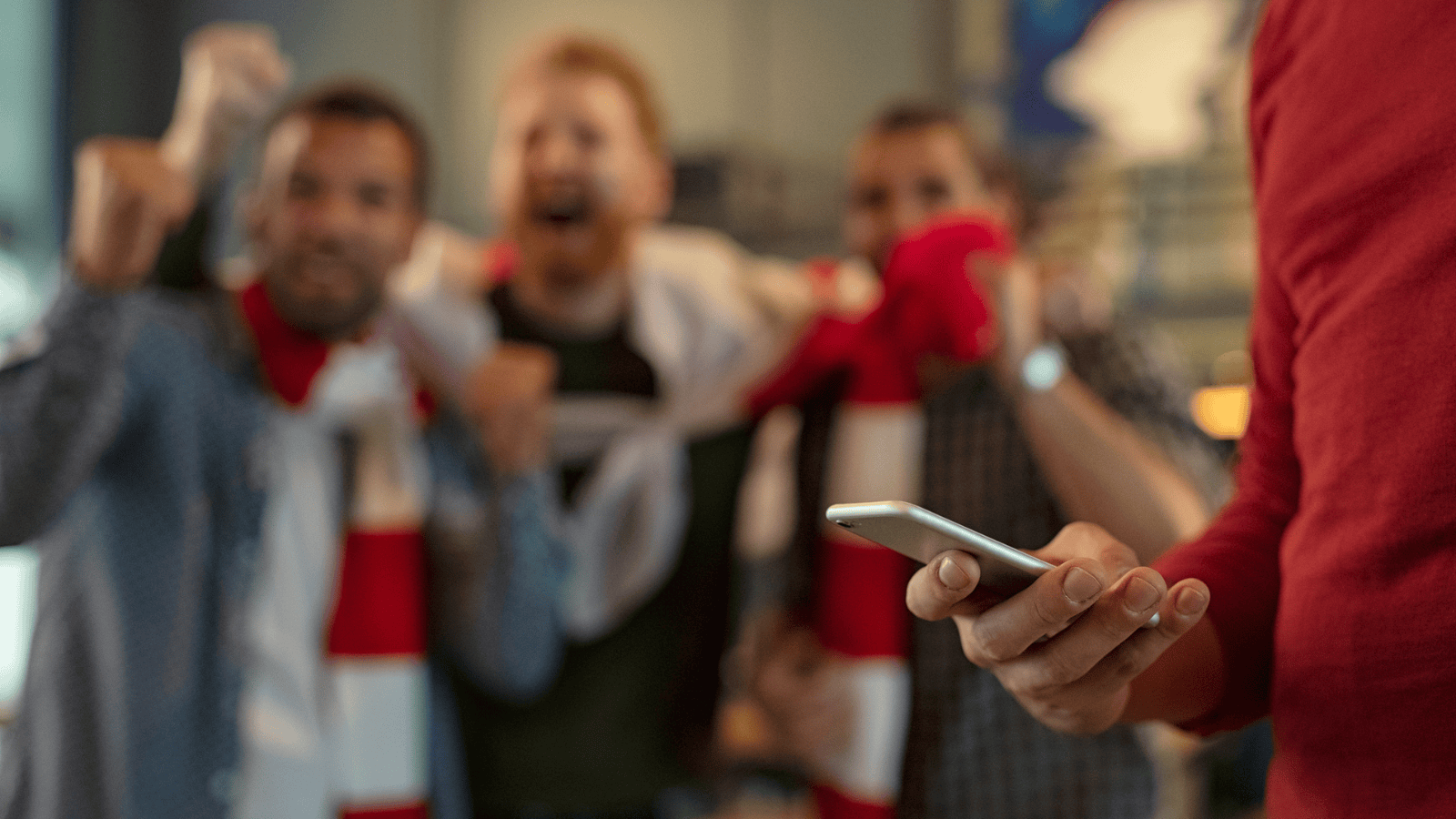 group of friends watching the football and celebrating with one person on their phone