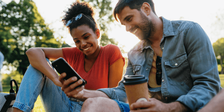 two people sat outside looking a phone smiling