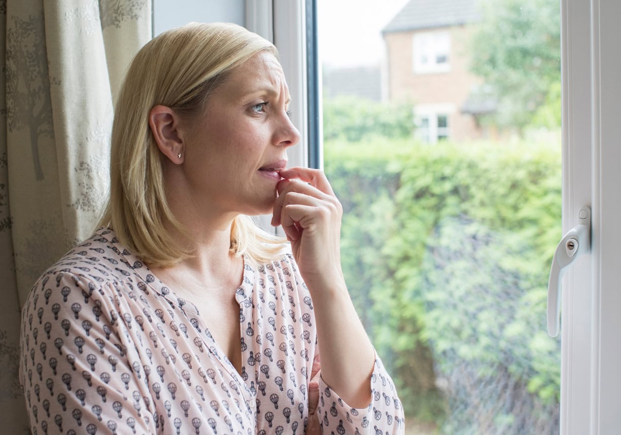 A worried woman looking out of the window.