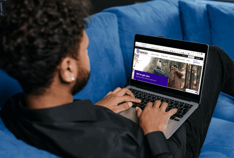 A man working on a laptop with the GamCare homepage visible