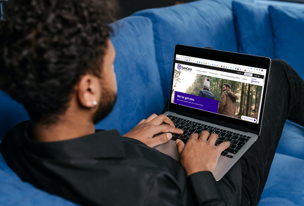 A man working on a laptop with the GamCare homepage visible